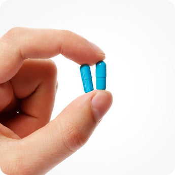 For Conceive Plus Maximum Fertility Bundle, close-up of two bright blue men's fertility support capsules held between fingers, highlighting capsule size, smooth texture, and dosage clarity against a clean white background.
