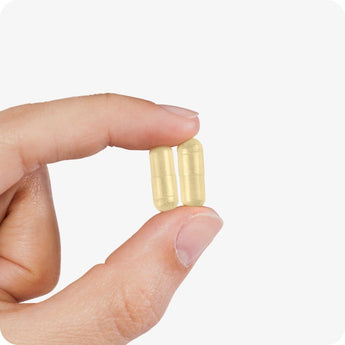 For Conceive Plus Maximum Fertility Bundle, close-up image of two pale yellow men's motility support capsules held between fingertips, illustrating capsule size and smooth finish designed for male fertility enhancement.