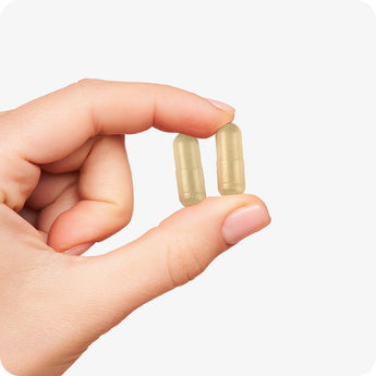 Conceive Plus Prenatal with DHA vegan capsules held between thumb and index finger to show actual capsule size and easy-to-swallow shape, presented on a light neutral background for clarity and product detail emphasis.