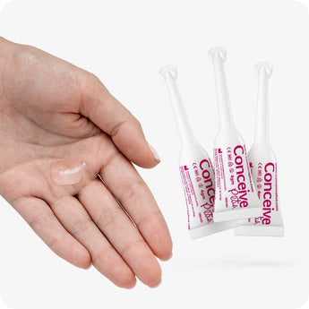 For Conceive Plus Women's Fertility Support and Fertility Lubricant Bundle, featuring three white 4g pre-filled fertility lubricant applicators with pink branding beside a female hand holding a dab of fertility lubricant gel, showcasing both product texture and applicator design on white background.